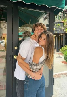 two people are hugging each other in front of a storefront with green awnings