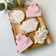 decorated cookies with pink and white frosting sitting on a wooden platter next to greenery