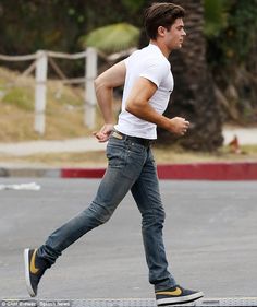 a man is running on the street with his foot in the air while wearing jeans and sneakers