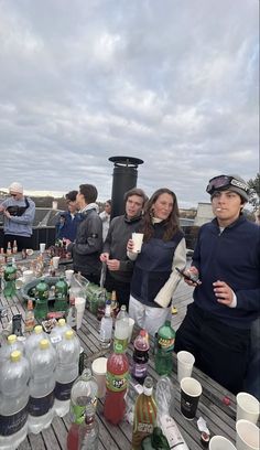 a group of people standing around a table filled with bottles and glasses on top of a wooden deck