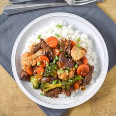 a white plate topped with meat and veggies on top of rice next to a fork