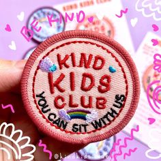 a hand holding a badge with the words kind kids club on it