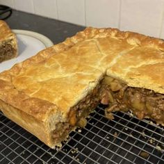 a meat pie sitting on top of a metal rack next to a plate with a slice cut out