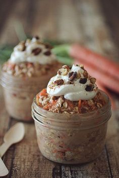 two jars filled with food sitting on top of a wooden table next to carrots