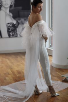 a woman standing in front of a painting wearing white pants and a long veil over her shoulders