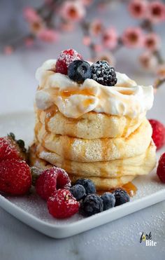 a stack of pancakes topped with whipped cream and berries on a white plate next to flowers