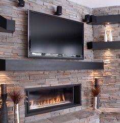 a television mounted on the wall above a fire place in a room with stone walls