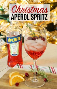 a christmas aperol spritz is served in a wine glass with an orange slice and rosemary garnish