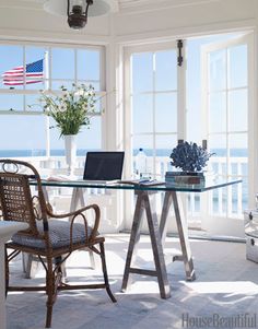 a laptop computer sitting on top of a glass table in front of two large windows