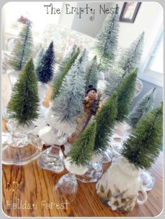 small christmas trees in clear glass vases on a wooden table with the words, the empty nest