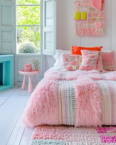 a bedroom with pink and white bedding, pillows and rugs on the floor