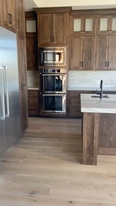 an empty kitchen with wooden cabinets and stainless steel appliances in the center, along with hardwood flooring