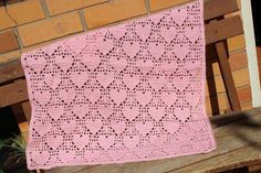 a pink crocheted blanket sitting on top of a wooden bench next to a brick wall