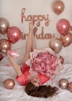 a woman laying on top of a bed holding a bouquet of flowers next to balloons