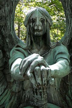 an angel statue sitting in the middle of a forest with its hands on his chest