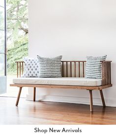 a wooden bench sitting in front of a window with pillows on it's back