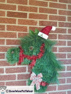 a teddy bear made out of fake grass on the side of a brick wall wearing a santa hat