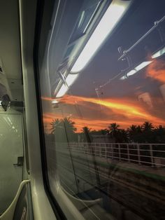 the sun is setting on an orange sky as seen from a train window with palm trees in the foreground