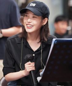 a woman sitting in front of a laptop computer while wearing a hat and holding a microphone