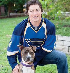 a man kneeling down next to a brown and white pit bull terrier in a hockey jersey