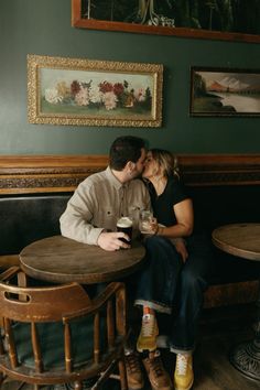 a man and woman sitting at a table with drinks in front of them, kissing