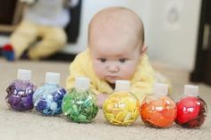 a baby laying on the floor next to seven small bottles filled with different colored candies