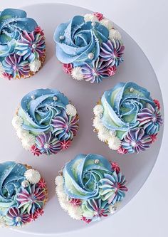 six cupcakes with blue frosting and pink flowers on a white platter