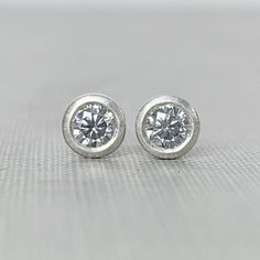 3 mm page grey moissanite stud earrings, bezel set in your choice of sterling silver or 14k gold. Choose from yellow, rose or white gold. May be ordered singly or in pairs. Sterling silver is pictured in the first three photos followed by 14k yellow gold and 14k white gold. These earrings are made to order and will ship within 3-5 days. They are TINY! (See photo in hand for scale.)DETAILS- 3 mm grey moissanite- bezel setting - satin finish- choice of solid 14k gold or sterling silver- clear plas Sterling Silver Single Diamond Earrings Gift, Gift Sterling Silver Single Diamond Earrings, Silver Earrings With Single Diamond For Gift, Silver Sterling Silver Diamond Earrings With Round Stone, Silver Earrings With Single Diamond For Anniversary, Everyday Round Earrings With Bezel Setting, White Gold Sterling Silver Bezel Set Diamond Earrings, Sterling Silver Single Diamond Round-cut Earrings, Minimalist Solitaire Sterling Silver Diamond Earrings