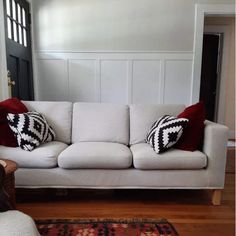 a white couch with red and black pillows on it in a living room next to a door