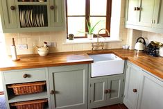 a kitchen with green cabinets and wooden counter tops, white walls and red tile flooring