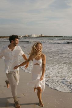 a man and woman are running on the beach holding hands as they run towards the water