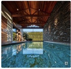 an indoor swimming pool with stone walls and wood ceilinging, surrounded by glass windows