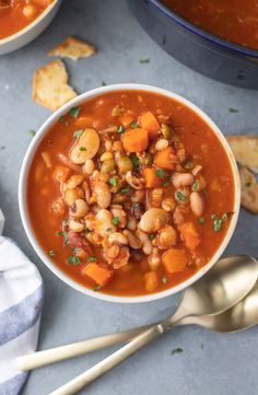 a white bowl filled with beans and carrots next to some crackers on the side