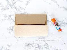 an empty cardboard box next to some markers on a marble counter with orange and blue pens