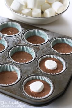 cupcake tins with marshmallows in them and a bowl of chocolate