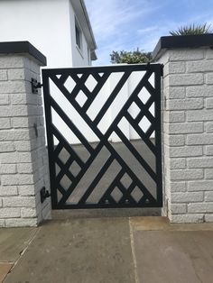 an iron gate in front of a white brick wall and concrete walkway with black accents