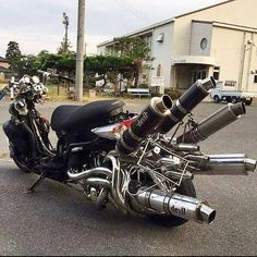 a black motorcycle parked in a parking lot next to a tall building with a large exhaust system on it's back end