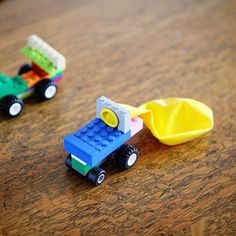 two legos are sitting on a table and one is carrying a yellow wheelbarrow