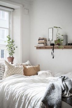 a bed with white sheets and pillows next to a window in a room filled with books