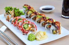 sushi rolls on a white plate with chopsticks next to it and a glass of black liquid