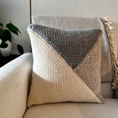 a white couch with two pillows and a potted plant in the corner next to it