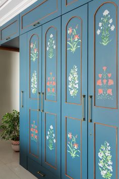 a blue cabinet with flowers painted on the side and gold trimmings, along with a potted plant