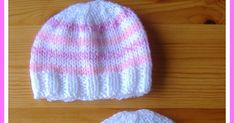 two white and pink knitted hats sitting on top of a wooden table next to each other