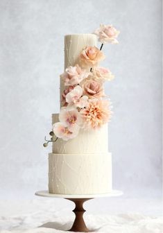 a three tiered wedding cake with pink flowers on the top and bottom, sitting on a white tablecloth