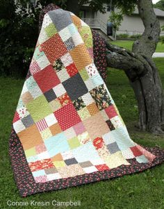 a quilted blanket sitting on the grass next to a tree