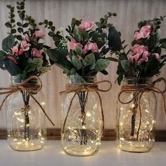 three mason jars with lights and flowers in them