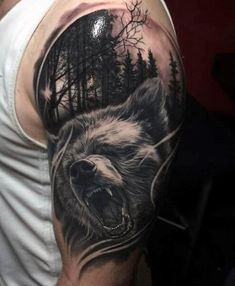 a man's arm with a bear and forest scene on the back of it