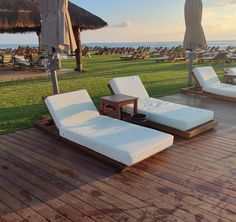 two chaise lounge chairs on a wooden deck overlooking the ocean and grass covered beach