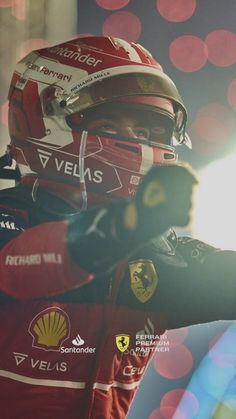 a man in a red racing suit and helmet pointing to the side with his right hand