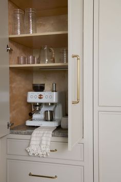 a kitchen with white cupboards and gold pulls on the doors, an espresso machine is in the corner